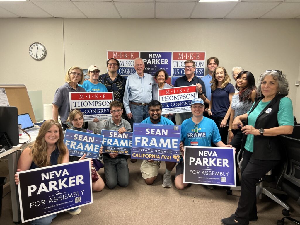 Group gathered indoors holding Democratic campaign signs.