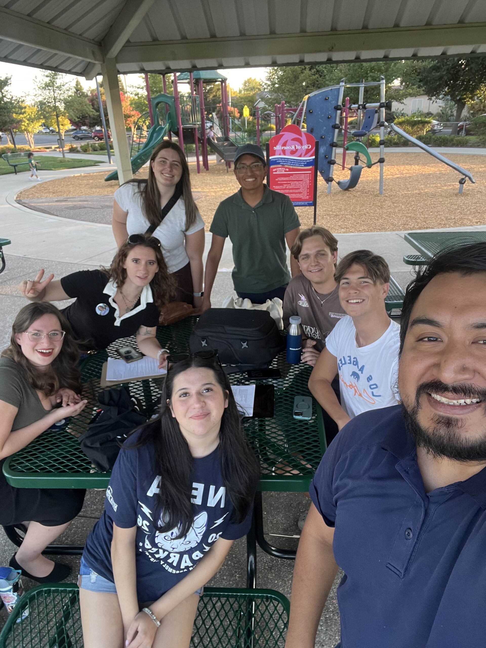 Students gathered around a picnic table at a park.